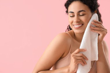 Genç Afro-Amerikalı kadın pembe arka planda havluyla makyajı temizliyor.