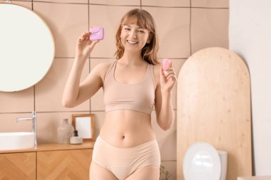 Tuvalette tampon kutusu ve regl bardağı olan genç bir kadın.