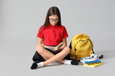 Gözlüklü küçük kız ışık arkaplanı üzerine kitap okuyor.
