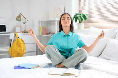 Küçük liseli kız yatak odasında çalışırken meditasyon yapıyor.