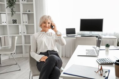 Ofiste cep telefonuyla konuşan olgun bir iş kadını.