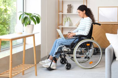 Evde dizüstü bilgisayarlı, tekerlekli sandalyedeki genç Afro-Amerikalı kadın.