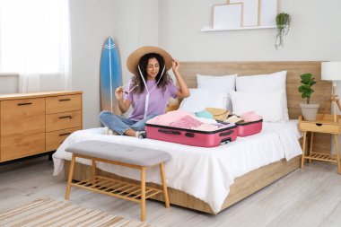 Genç Afro-Amerikalı bir kadın otel odasında bavulunu giysileriyle açıyor.