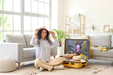 Genç Afro-Amerikalı kadın otel odasında seyahat aksesuarlarıyla bavulunu boşaltıyor.