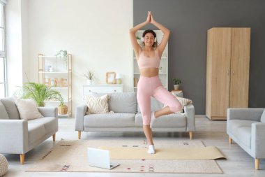 Dizüstü bilgisayarı ve kulaklığı olan, evde yoga yapan Afro-Amerikalı bir kadın.