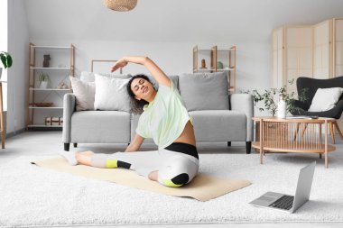 Laptopuyla evde yoga minderinde pilates yapan Afro-Amerikalı bir kadın.