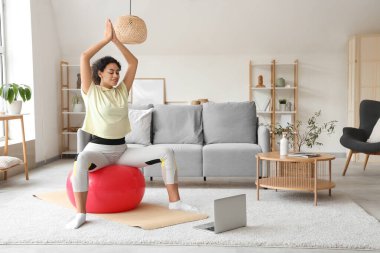 Laptopuyla evde yoga yapan Afro-Amerikalı bir kadın.