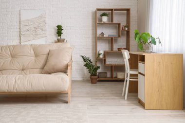 Pencerenin yanında beyaz kanepe ve çalışma alanı olan aydınlık oturma odasının içinde.