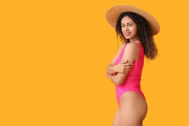 Zarif pembe mayo ve sarı arka planda hasır şapkalı güzel Afro-Amerikan kadın.