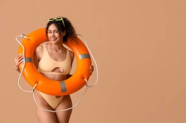 Kahverengi arka planda can simidi olan şık mayolu güzel bir Afro-Amerikalı kadın.