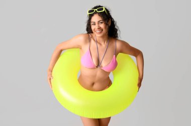 Gri arka planda şişirilebilir yüzüğü olan zarif pembe mayolu güzel bir Afro-Amerikalı kadın.