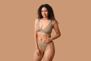 Güzel, mutlu, bej arka planda iç çamaşırlı Afro-Amerikan kadın.