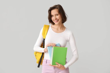 Sırt çantası ve gri arka planda defterleri olan mutlu kız öğrenci.