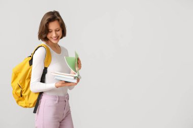 Gri arkaplan üzerine not defterleri ve sırt çantasıyla güzel bir kız öğrenci.