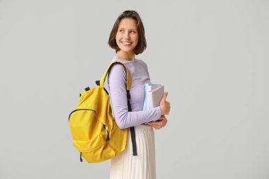 Sırt çantası ve gri arka plan kitapları olan güzel bir kız öğrenci.