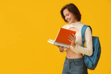Sarı arka planda not defterleri ve sırt çantasıyla güzel bir kız öğrenci.