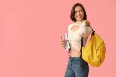 Sırt çantası ve pembe arka plan kitapları olan güzel bir kız öğrenci.