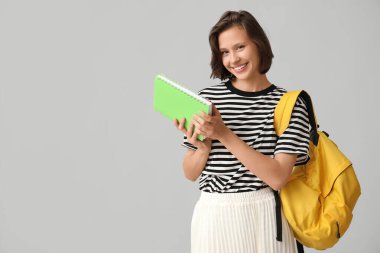 Gri arka planda sırt çantası ve defteri olan güzel bir kız öğrenci.