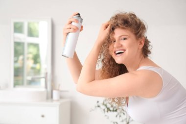 Evdeki banyoya saç spreyi sıkan genç ve güzel bir kadın.