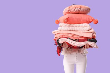 Mor arka planda farklı battaniye ve yastıklar yığını olan güzel genç bir kadın.