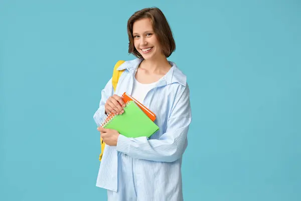 Beautiful female student with notebooks on blue background