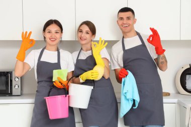 Kovalarla ve temizlik malzemeleriyle dolu bir grup genç hademe mutfakta iyi görünüyor.