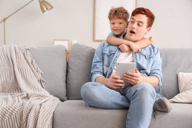 Küçük çocuk evde babasına tablet bilgisayarla sarılıyor.