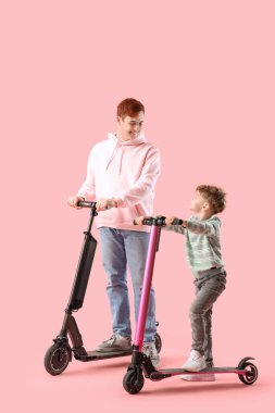 Pembe arka planda elektrikli scooter kullanan babasıyla küçük bir çocuk.
