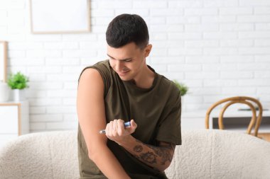 Şeker hastası genç adam evde tükenmez kalem kullanıyor.