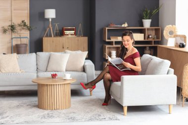 Oturma odasında dergi okuyan güzel bir kadının portresi.