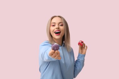 Pembe arka planda tatlı badem kurabiyeleri olan mutlu genç bir kadın.