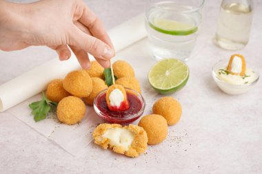 Hafif arkaplanda tatlı soslu kızarmış mozarella topları yiyen bir kadın.