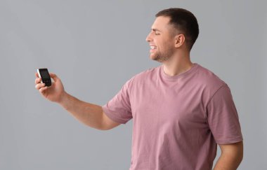 Gri arka planda glukometresi olan yakışıklı genç, mutlu diyabetik adam.