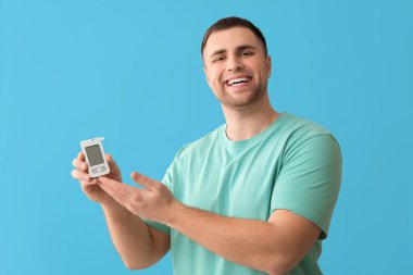 Yakışıklı genç, mutlu diyabetik adam mavi arka planda kan şekeri seviyesini kontrol ediyor.