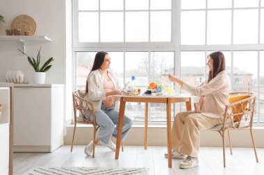 Hamile bayan arkadaşlar ve mutfak masasında bebek kıyafetleri.