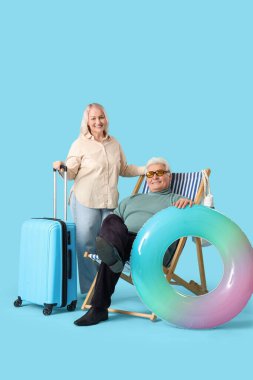 Çantalı ve yüzme yüzüklü olgun çift mavi arka planda yaz tatiline hazır.