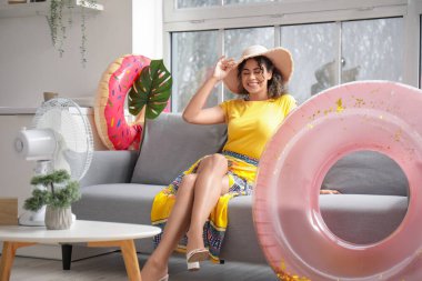 Hasır şapkalı gülümseyen Afro-Amerikan genç kadın oturma odasında şişme yüzüklerle oturuyor.