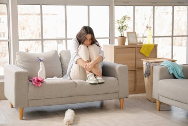 Oturma odasını temizledikten sonra kanepede oturan yorgun genç kadın.