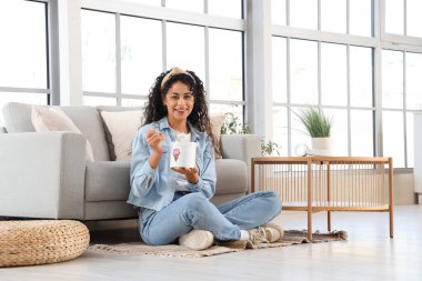 Oturma odasında bir sepet dondurması olan güzel bir Afro-Amerikalı kadın.