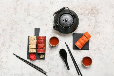 Lezzetli suşi ruloları, yemek çubukları, çaydanlık ve beyaz grunge arka planda bir fincan çay.