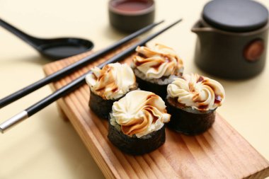 Açık sarı arka planda lezzetli suşi ruloları ve çubukları olan tahta, yakın plan.