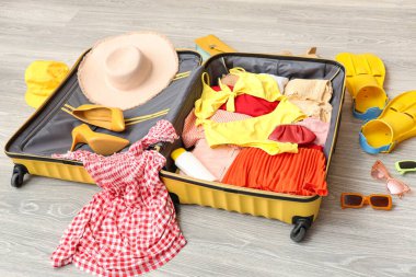 İçinde kadın kıyafetleri, güneş kremi ve yüzgeçler olan açık bir bavul. Seyahat kavramı