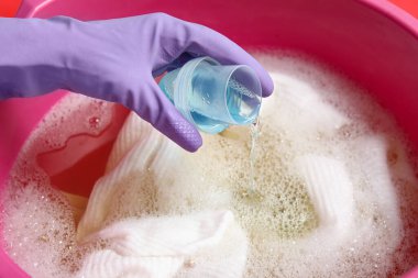 Lastik eldivenli kadın kırmızı arka plandaki plastik leğende çamaşırlara deterjan ekliyor.