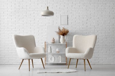 Rahat koltuklar, raf ünitesi ve beyaz tuğla duvarın yanındaki dekorasyon.