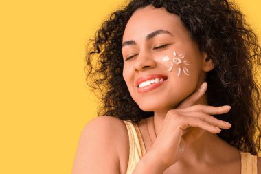 Sarı arka planda güneş kreminden yapılmış genç bir Afro-Amerikalı kadın, yakın plan.