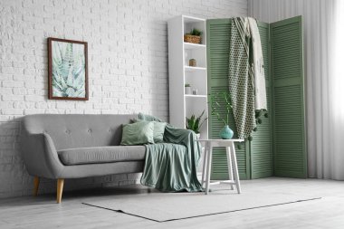 Şık oturma odasının içinde rahat kanepe, raf ünitesi ve katlanır ekran var.