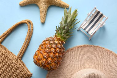 Hasır şapkalı, çantalı, deniz yıldızlı ve mavi arka planda güverte sandalyesi olan taze ananas.