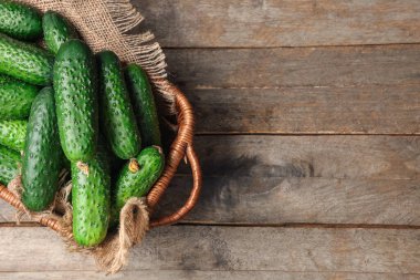 Tahta arka planda taze yeşil salatalıklı hasır sepet.