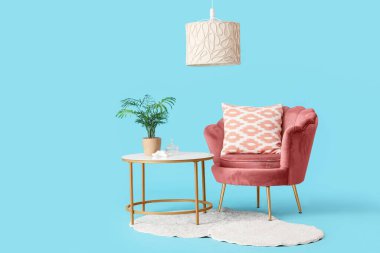 Masanın yanında yastıklı, mavi arka planda bitki olan rahat bir koltuk.