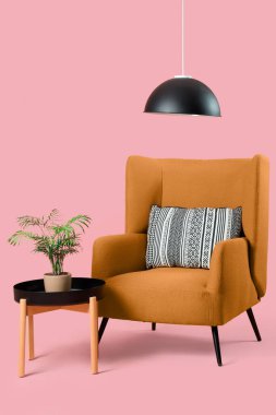 Yastıklı rahat koltuk ve pembe arka planda bitki örtüsü olan kahve masası.